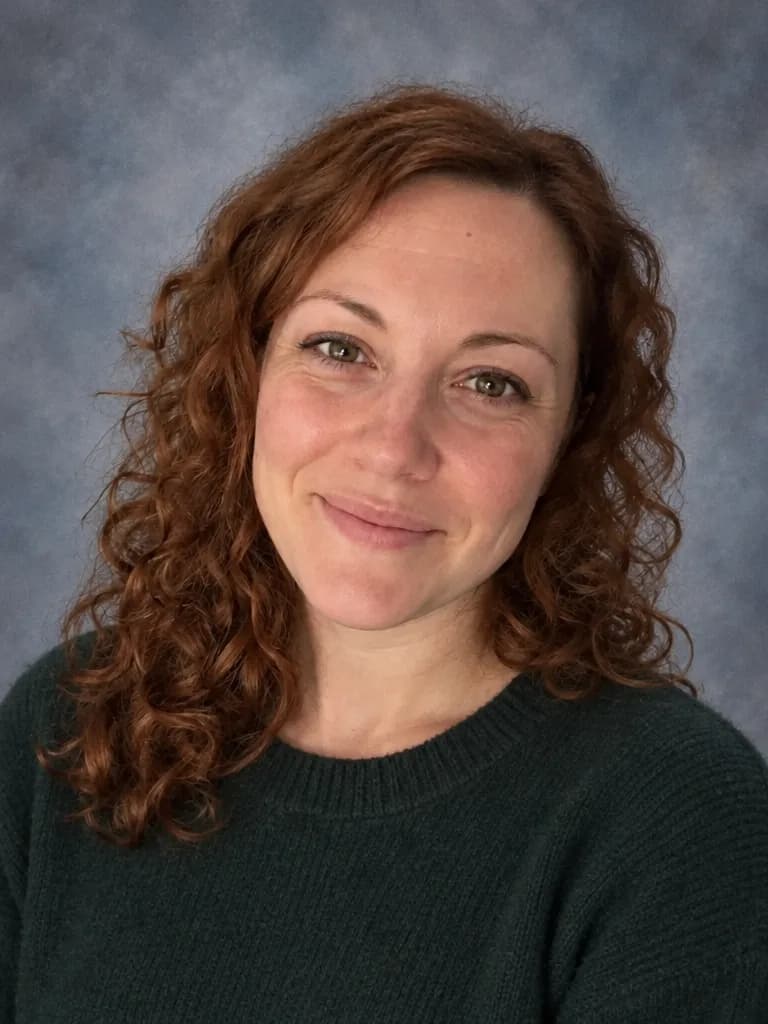 La misma mujer con un suéter verde oscuro ante un fondo jaspeado gris azulado de retrato escolar