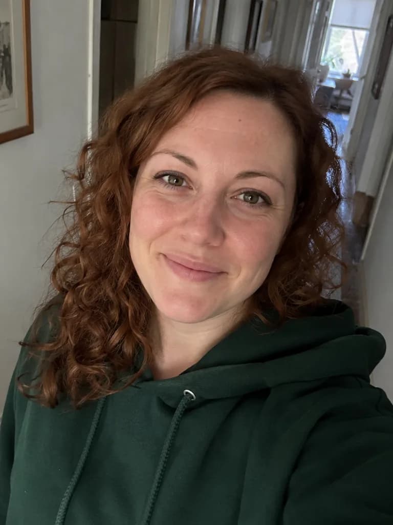 Selfie de una mujer de pelo rizado castaño rojizo con una sudadera verde en un pasillo