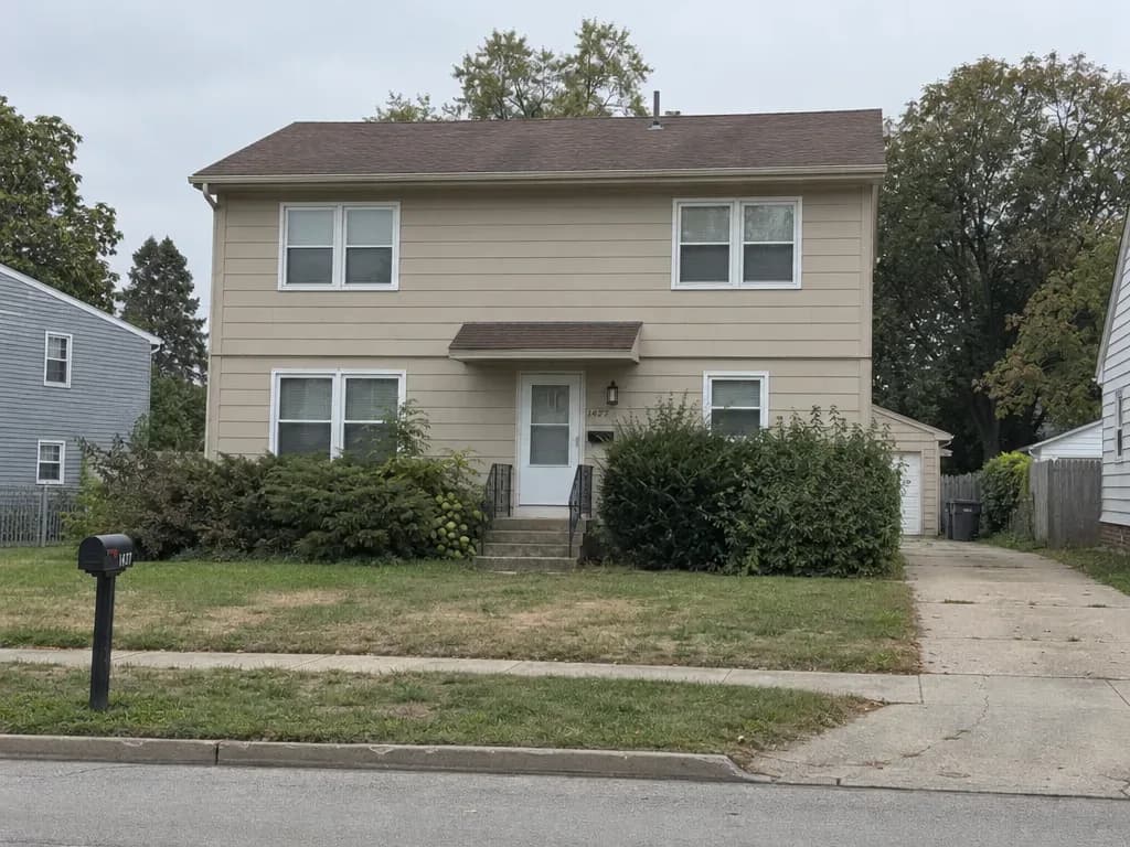 A two-story house with beige siding, an open front lawn, a mailbox and a concrete driveway