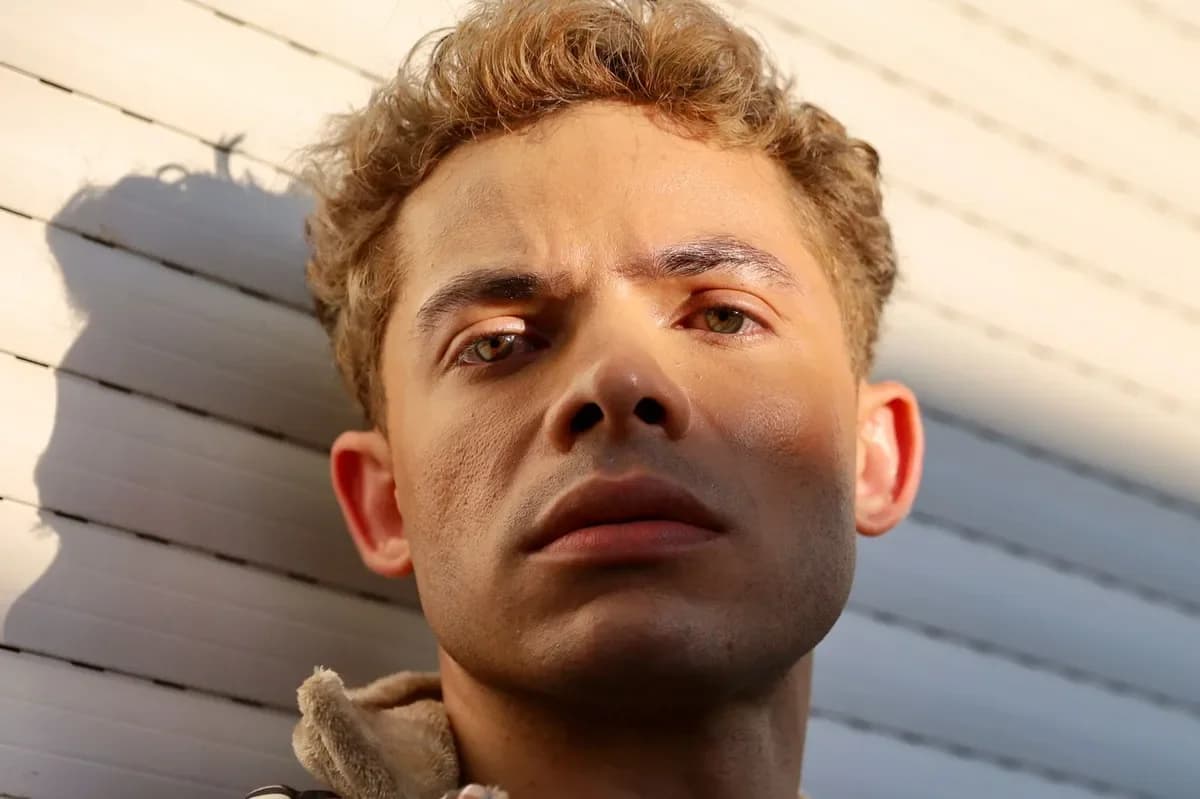 Curly-haired man against a light wall, part of his face in hard sun shadow