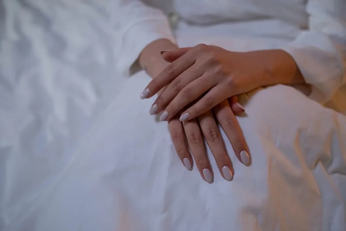 Folded hands on white sheets with nude nails