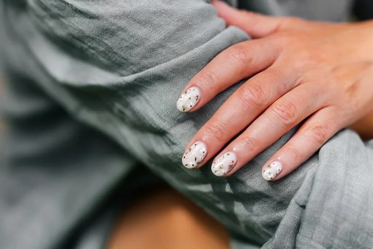 The same hand with milky nails and tiny painted flowers