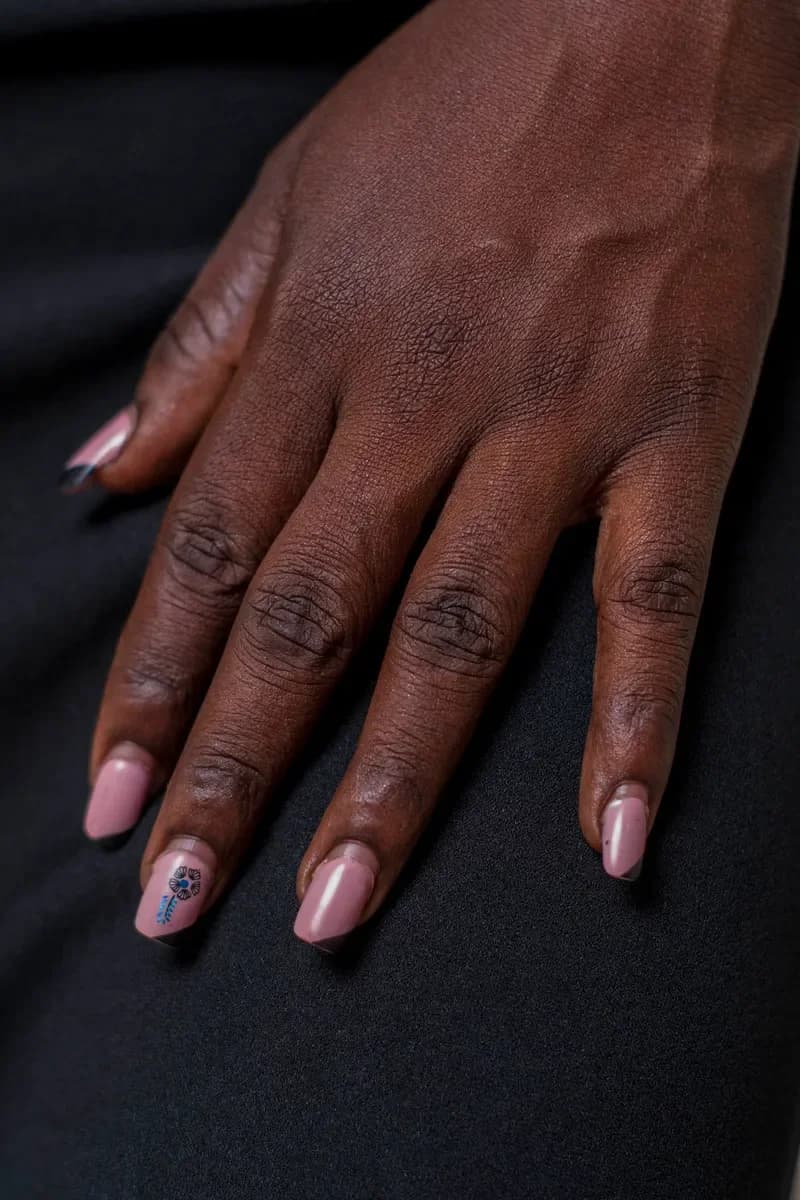 Hand with deep skin tone and pink almond nails on black fabric