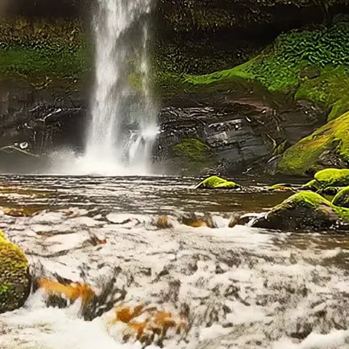 A forest waterfall with mossy rocks and churning water, a crop from the 1080p original with sharp spray and moss